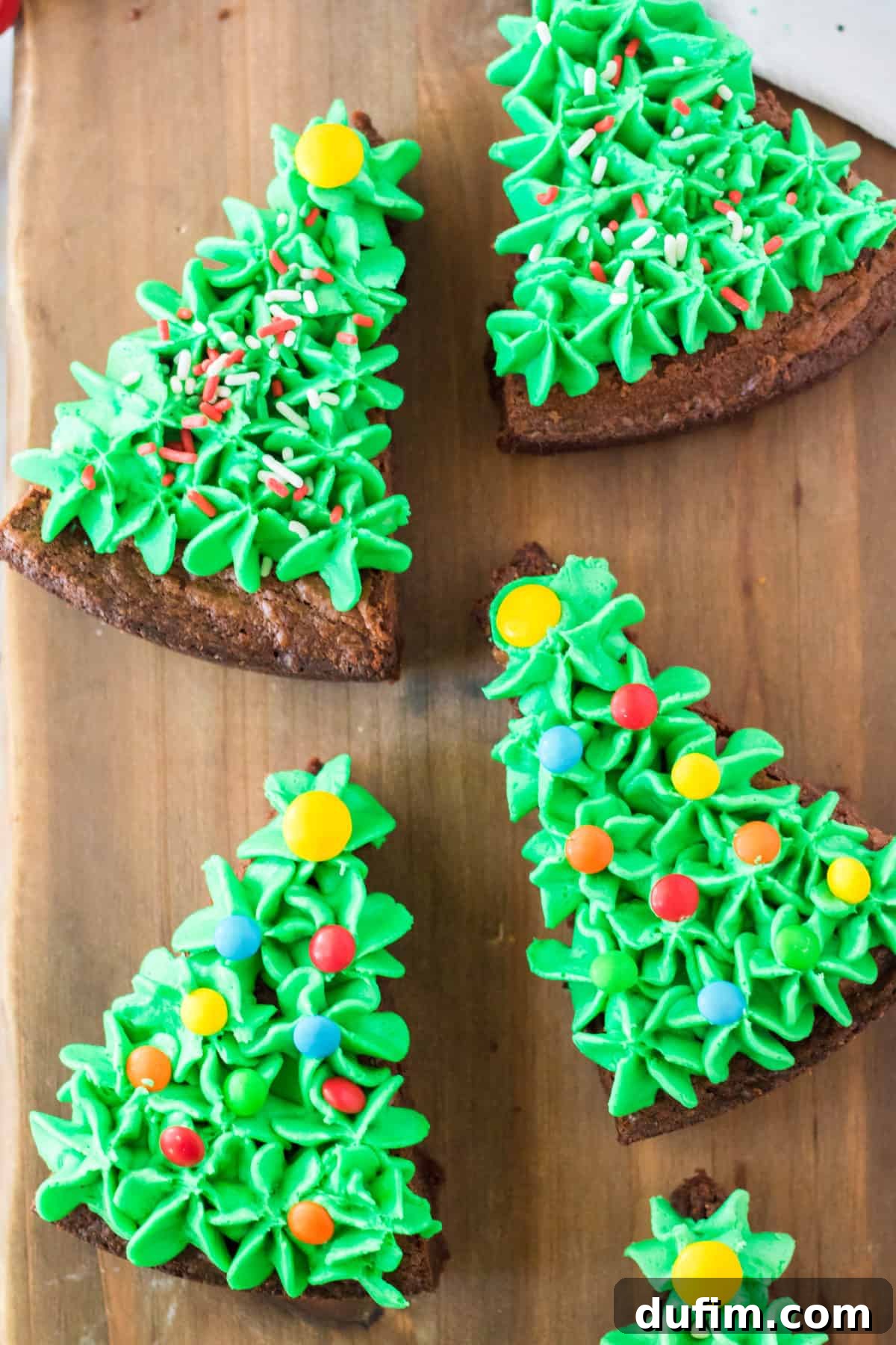 brownies cut into triangles and frosted with green frosting and sprinkles to look like Christmas trees on wooden background
