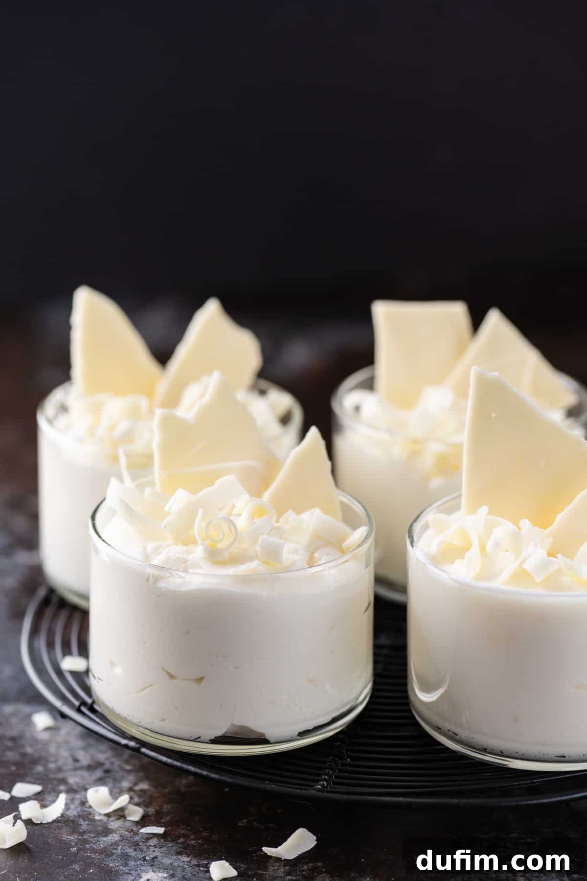 Four glass cups filled with luscious white chocolate mousse on a dark background, ready to be served or garnished.