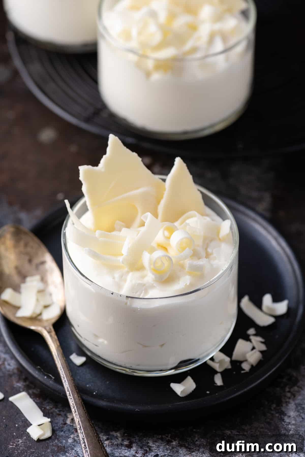 white chocolate mousse in small glass dish on dark plate and dark background