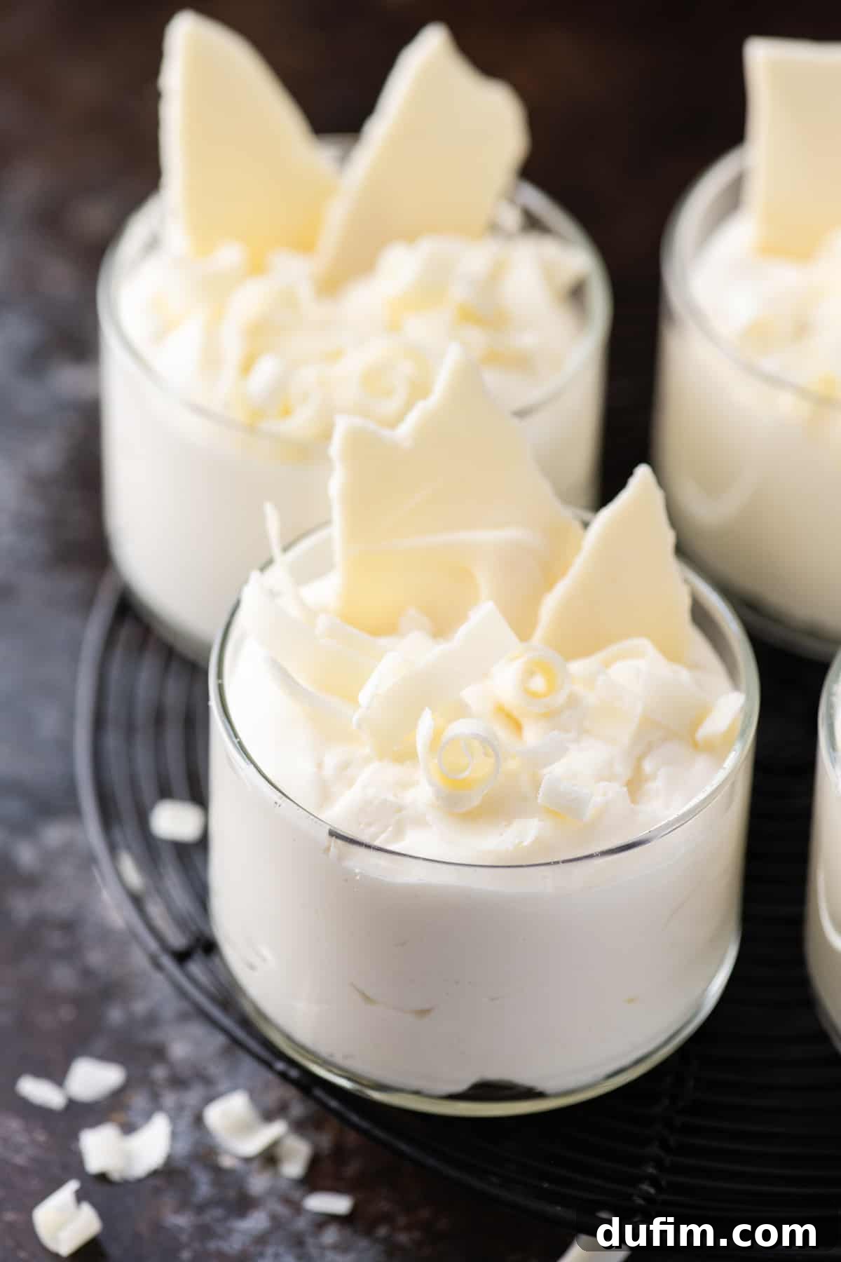Indulgent White Chocolate Mousse 6 A single serving of luxurious white chocolate mousse in a clear glass dish, beautifully placed on a dark plate against a muted, dark background.