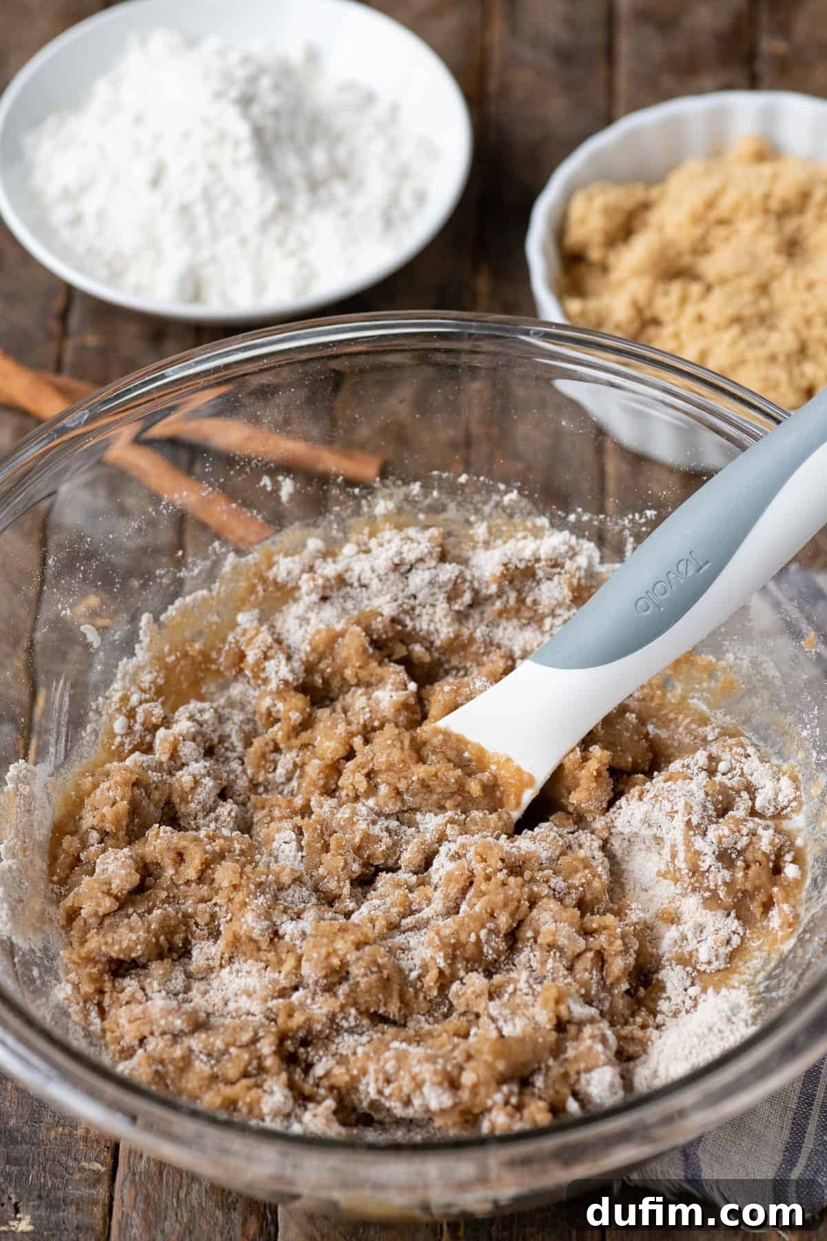A generous pile of finished crumb topping rests invitingly in a glass bowl on a textured wooden surface.