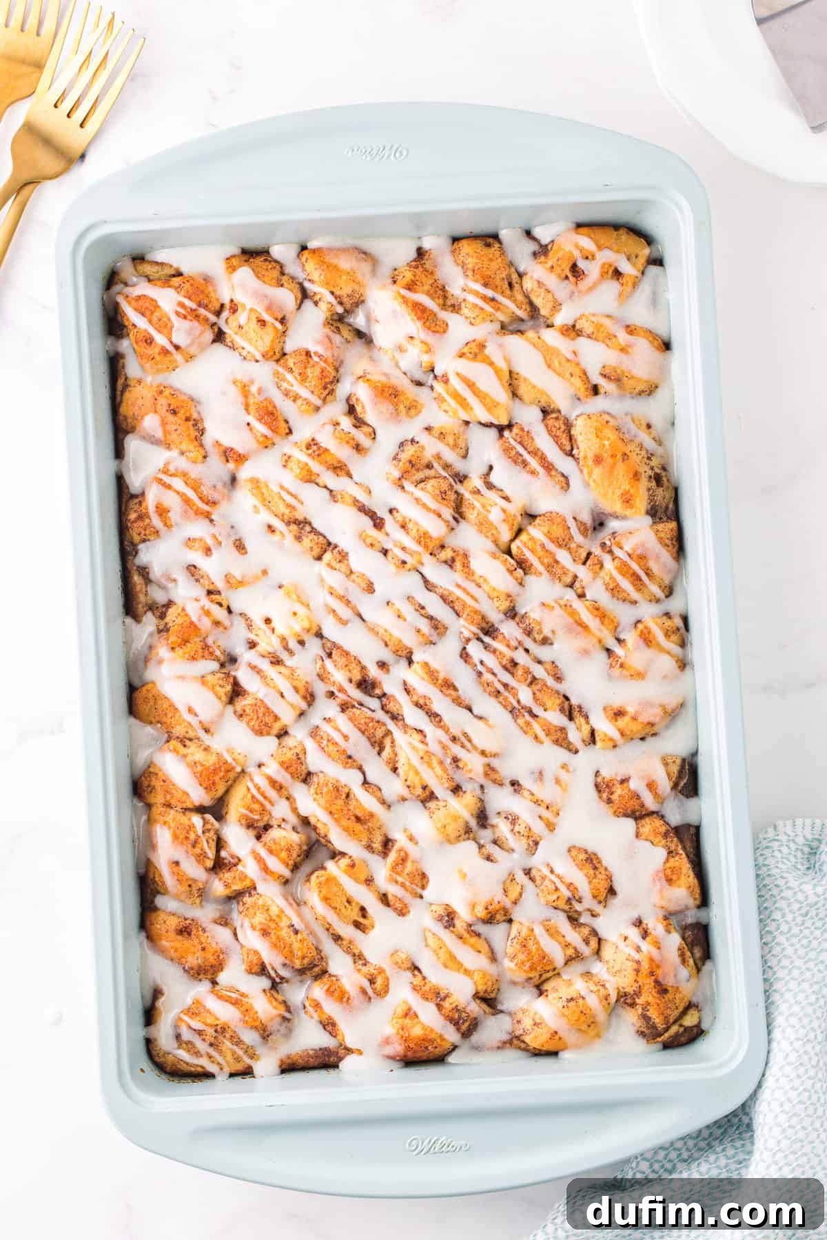 Cinnamon roll casserole with sweet white icing generously drizzled on top, served in a light blue baking dish. The rolls are golden brown and perfectly baked.