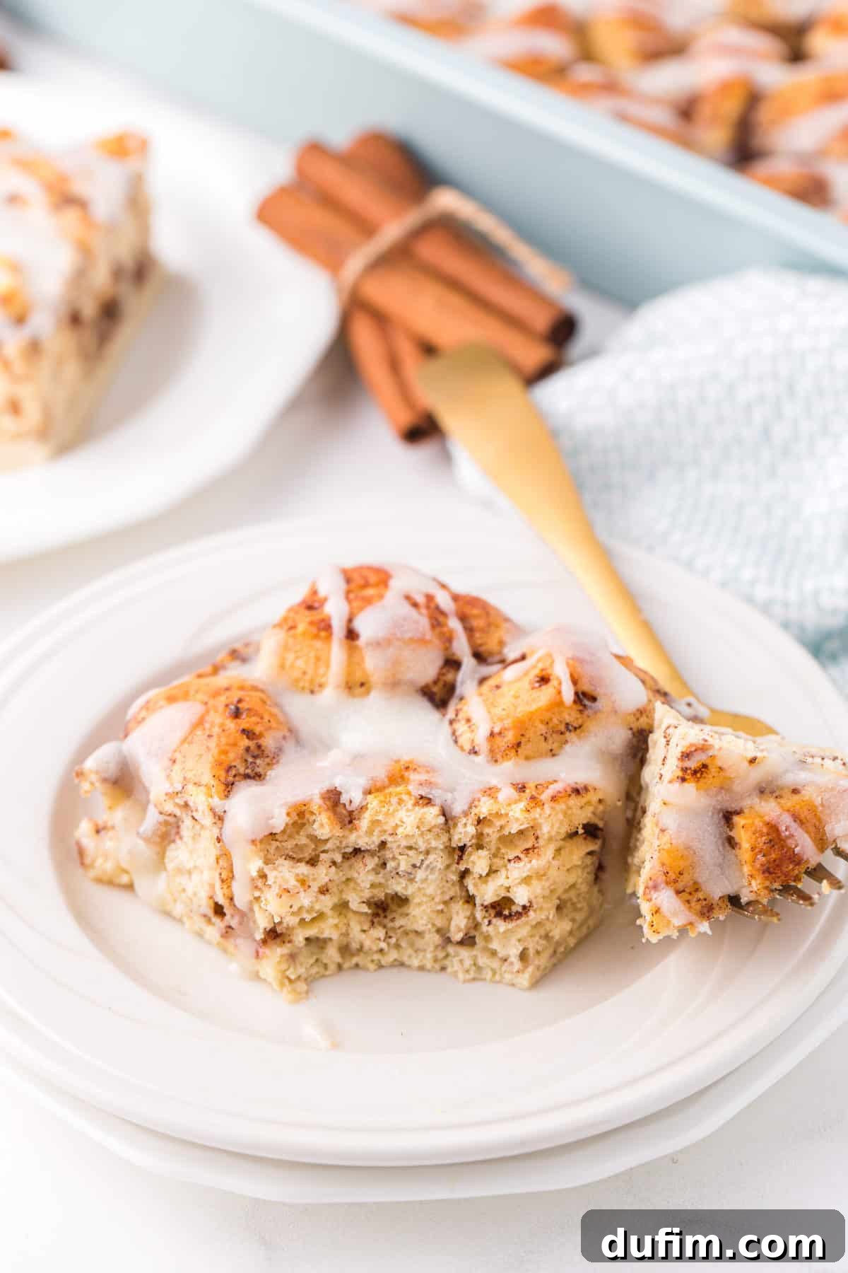 A delectable slice of cinnamon roll casserole, generously coated in sweet white icing, served on a white plate with a subtle blue pattern.