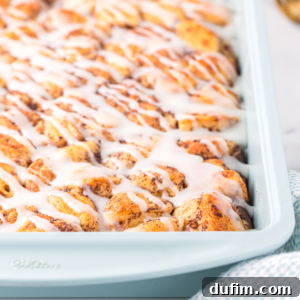 A close-up of a cinnamon roll casserole showcases golden-brown rolls packed together, generously drizzled with white icing. The soft, fluffy breakfast casserole looks irresistibly sweet and ready to enjoy.