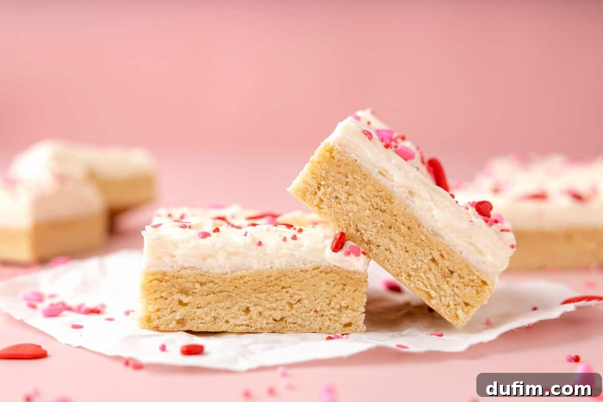 Sweetheart Sugar Cookie Bars 2 Two soft Valentine’s Day sugar cookie bars with white frosting and pink and red sprinkles on a festive pink background, perfect for a romantic treat.