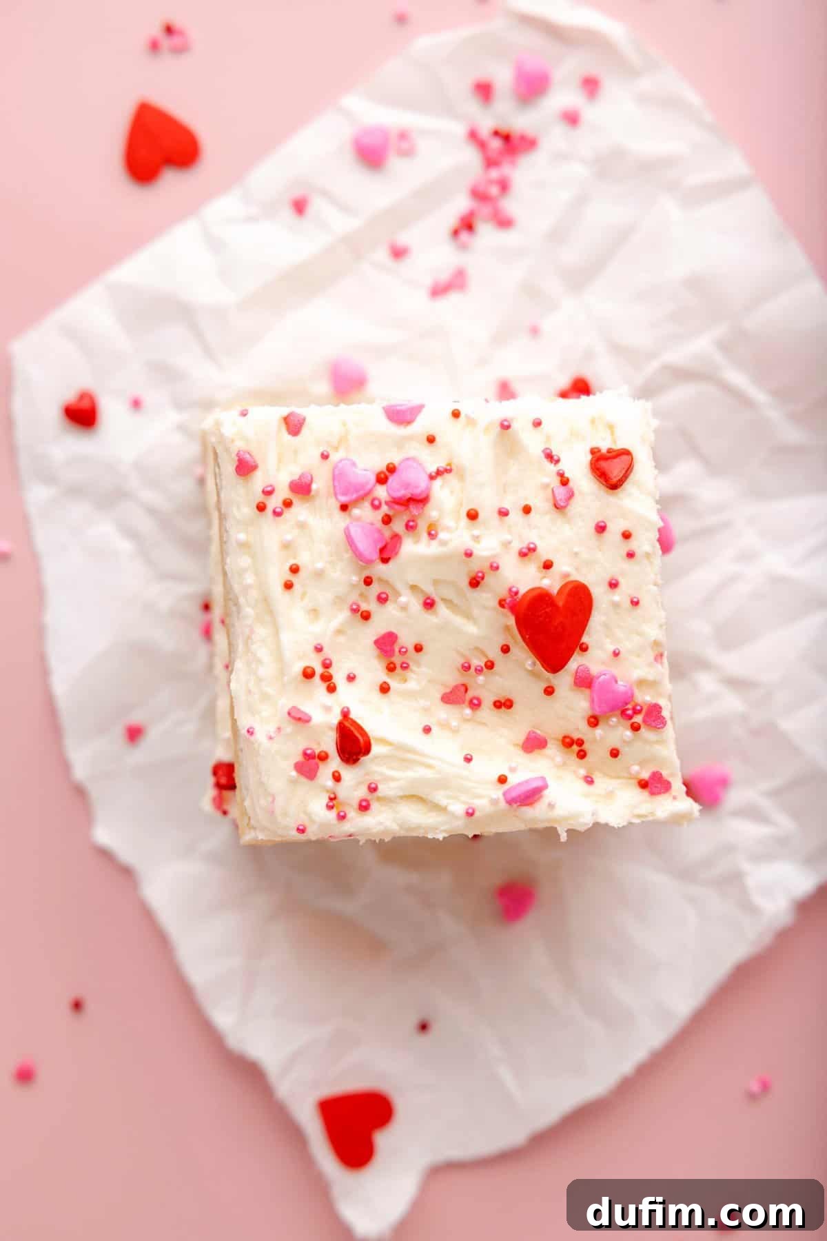 Sweetheart Sugar Cookie Bars 3 Two perfectly baked and frosted sugar cookie bars, adorned with Valentine's Day sprinkles, resting on a pink surface.