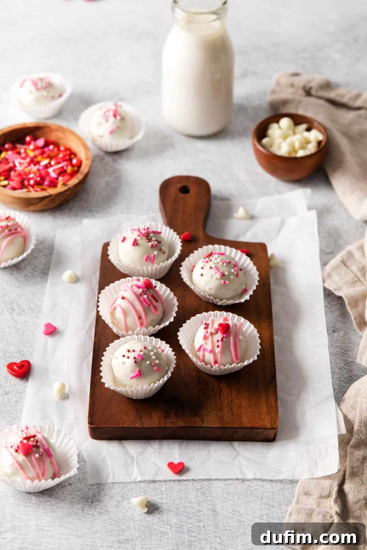 Velvety Red Cake Pop Delights 2 Delicious red velvet cake pops arranged neatly on a rustic wooden tray, set against a clean white background, garnished with festive sprinkles.