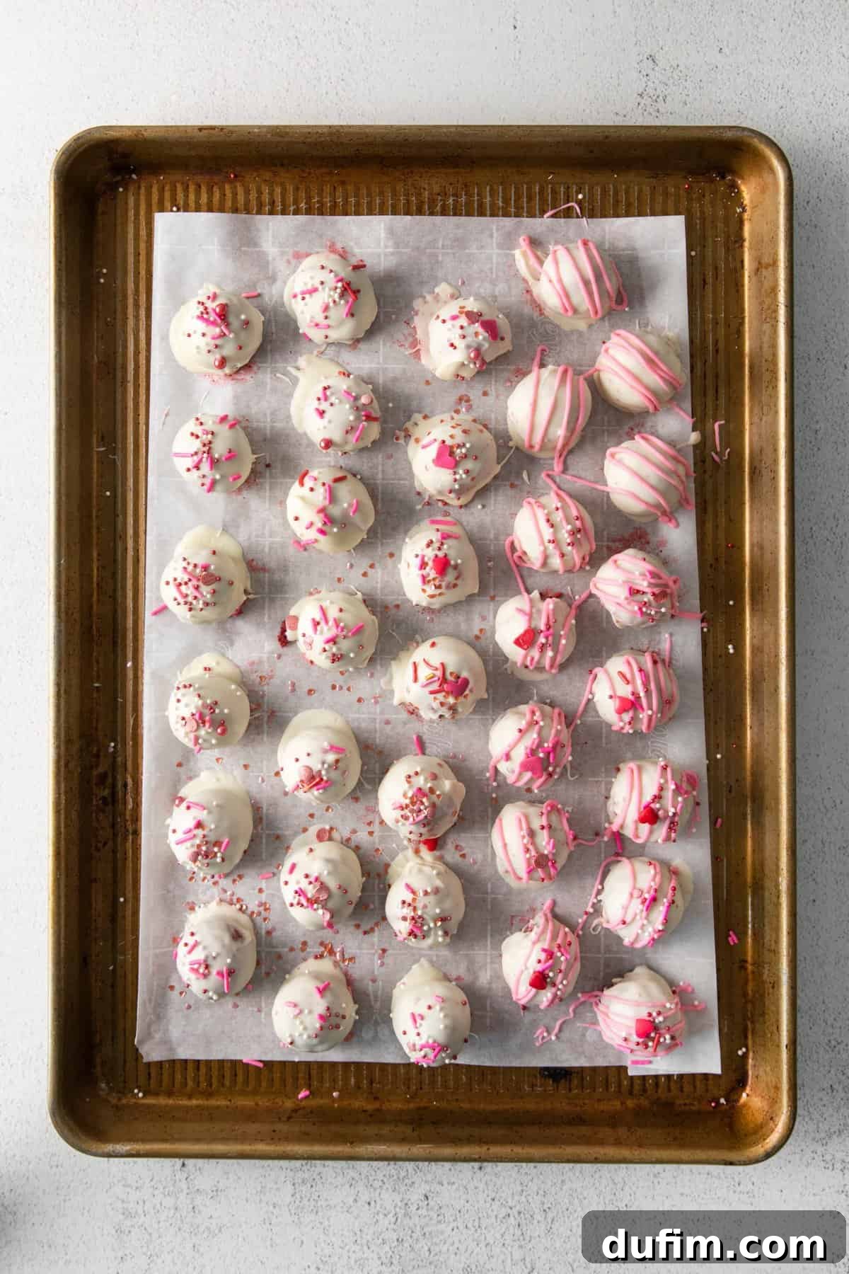 Velvety Red Cake Pop Delights 4 Freshly dipped red velvet cake pops coated in white chocolate and adorned with festive sprinkles, cooling on a metal baking sheet.