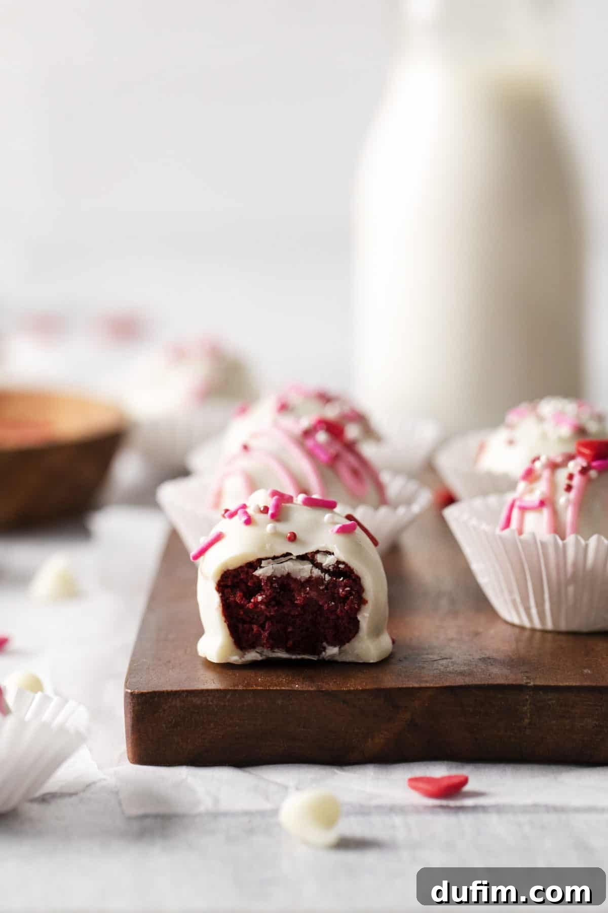 Velvety Red Cake Pop Delights 5 A perfectly dipped red velvet truffle with a single bite removed, showcasing its moist interior, resting on a wooden tray against a white backdrop.