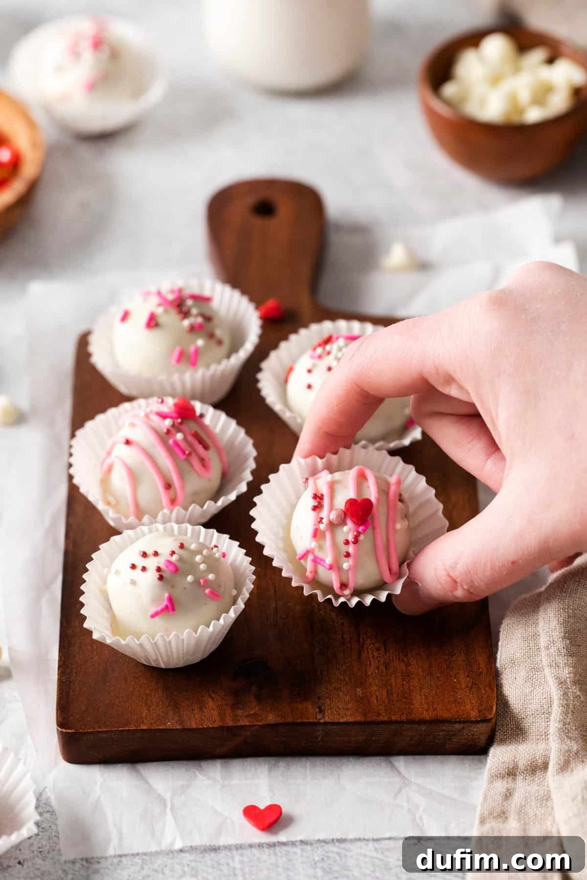 Velvety Red Cake Pop Delights 6 A selection of red velvet cake pops, some with white chocolate coating and festive sprinkles, presented on a wooden tray.