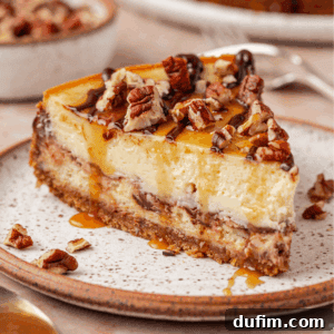 A slice of cheesecake with a crumbly crust, topped with chopped pecans and drizzled with caramel and chocolate sauce, sits on a ceramic plate.
