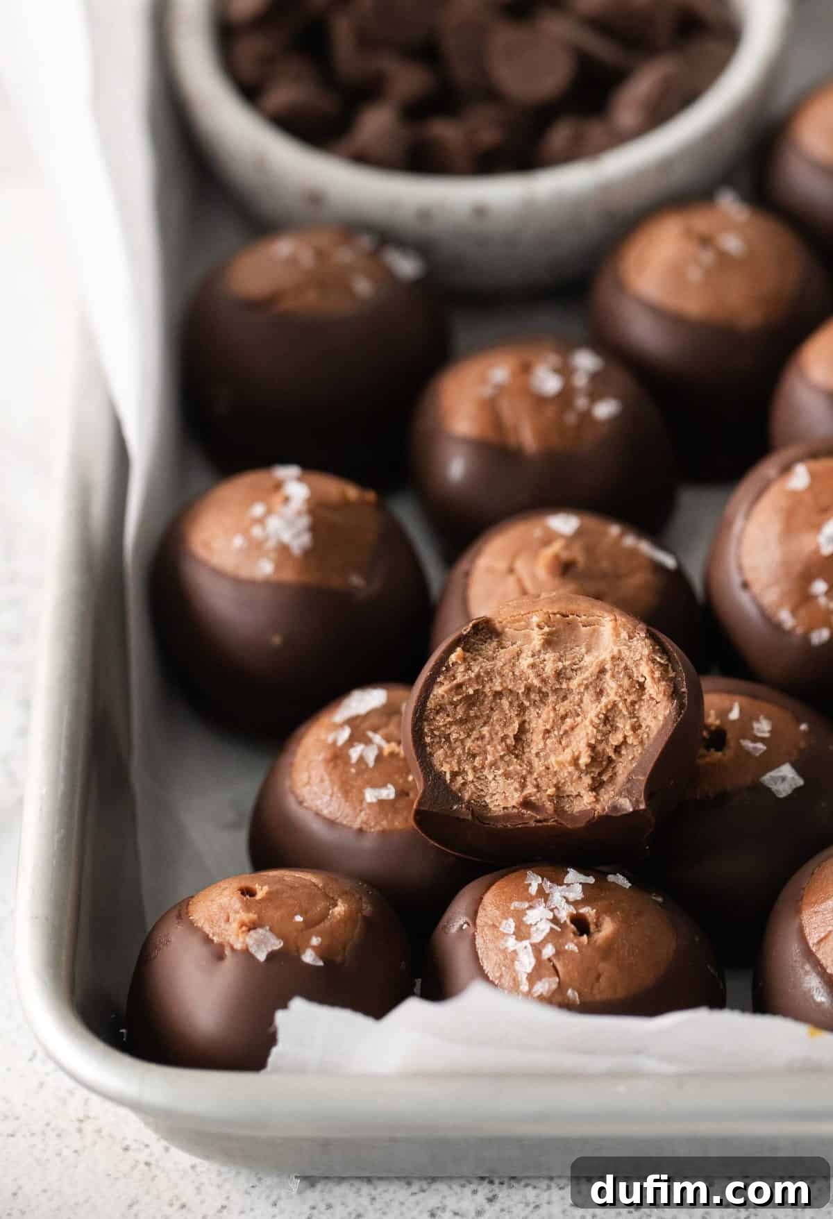 Decadent Nutella Buckeye Bites 4 Neatly arranged Nutella buckeye balls, partially dipped in chocolate, on a metal baking sheet with white parchment paper, showcasing their signature 'eye' design.