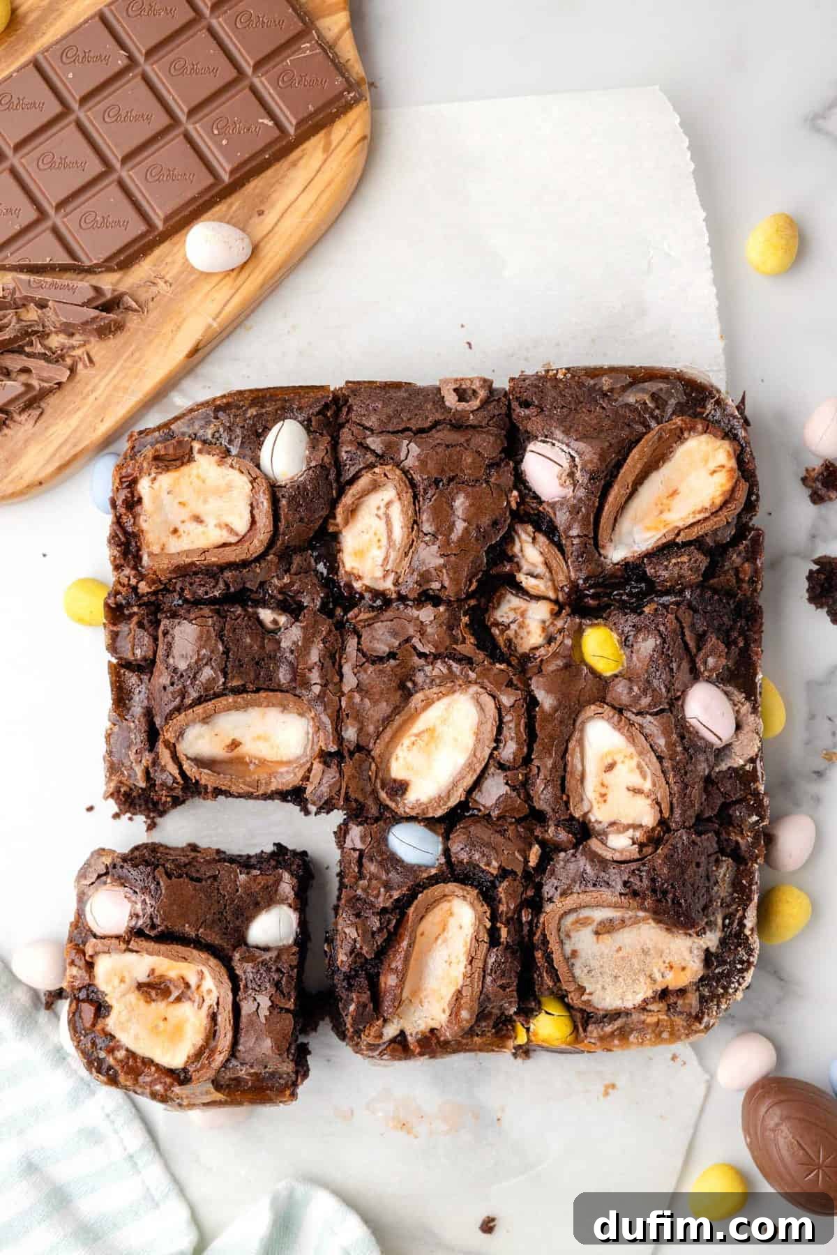 A batch of Cadbury Creme Egg Brownies in a glass pan, showcasing their fudgy texture and festive toppings, with a few pieces already cut out.