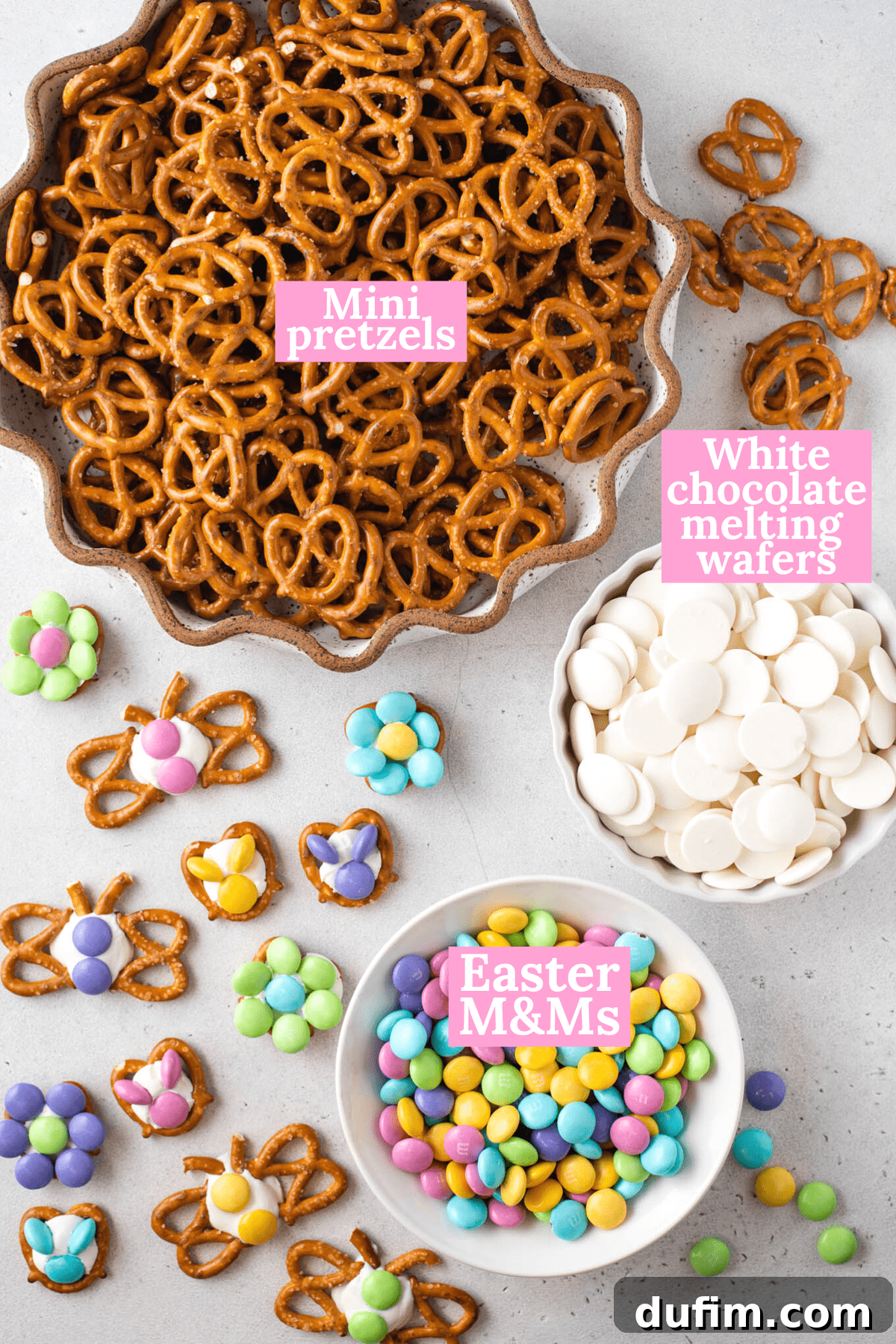 A flat lay photograph displaying the three essential ingredients for making Easter pretzels: a bag of mini pretzels, white candy melting wafers, and a bag of colorful Easter M&M's, all arranged on a light background.
