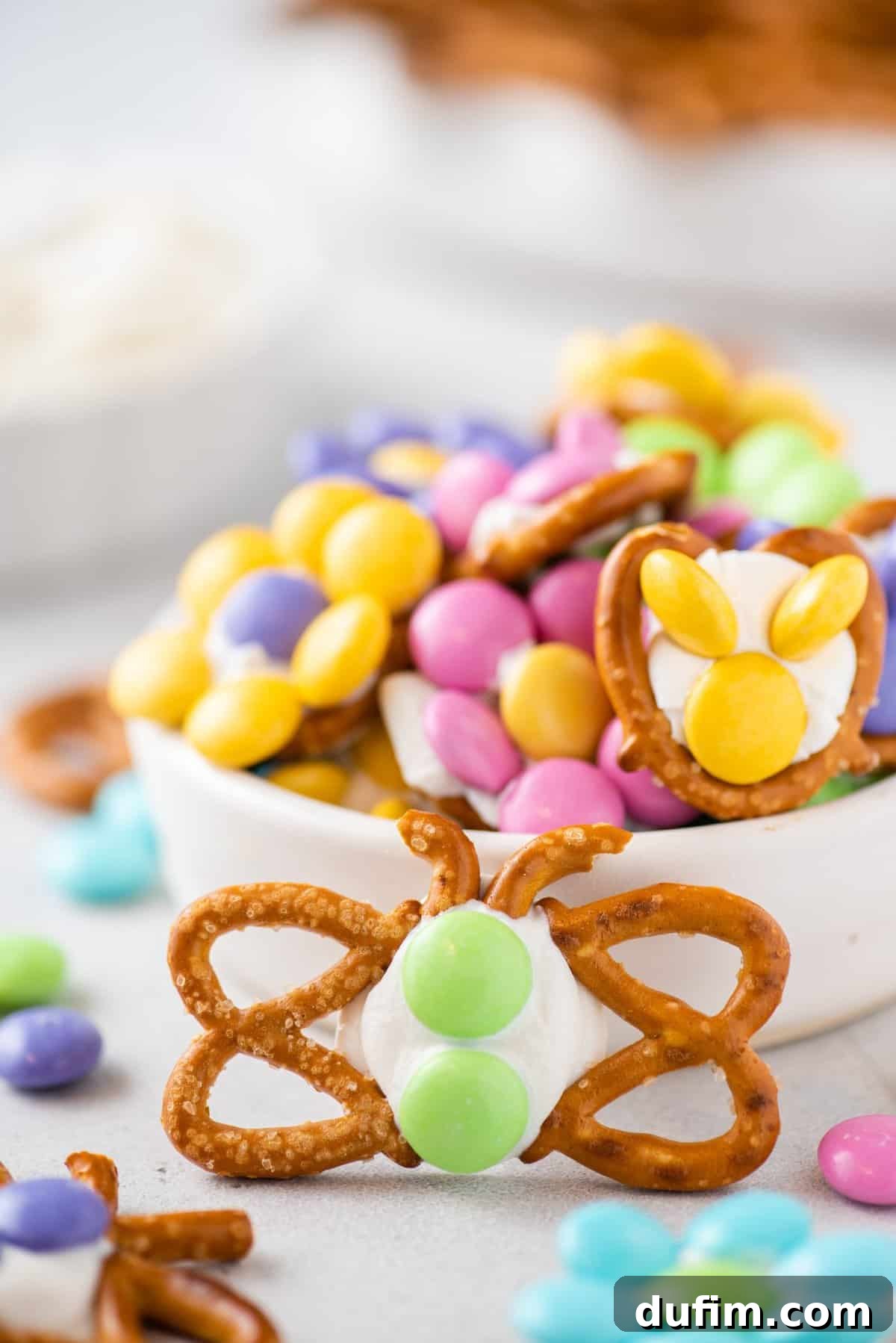 Close-up of a single, beautifully crafted pretzel butterfly propped elegantly on a white dish, highlighting its delicate pretzel wings and colorful M&M body.