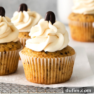 A close-up of Coffee Cupcakes with creamy swirled frosting and a chocolate coffee bean on top, placed on parchment paper and a cooling rack.