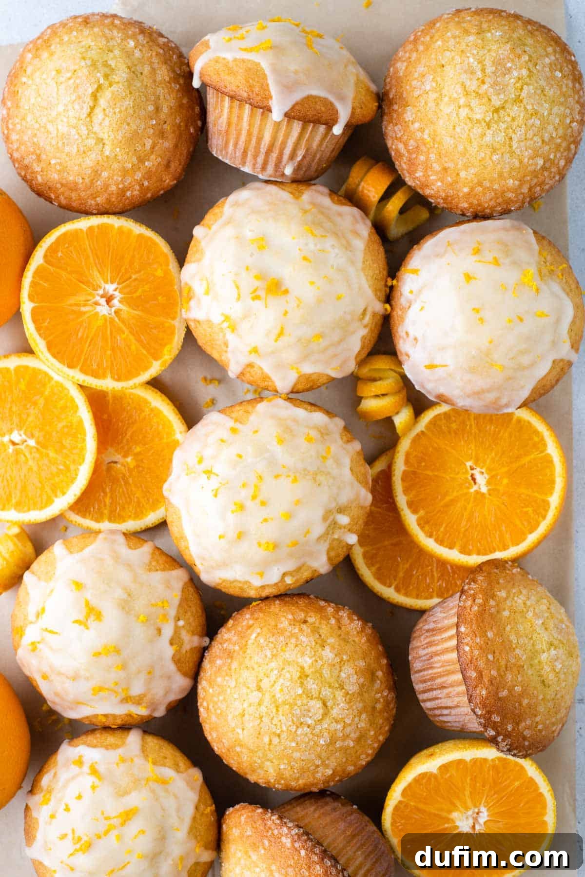 Freshly baked bakery style orange muffins arranged in a grid pattern, garnished with bright orange slices, showcasing their golden tops and inviting texture.