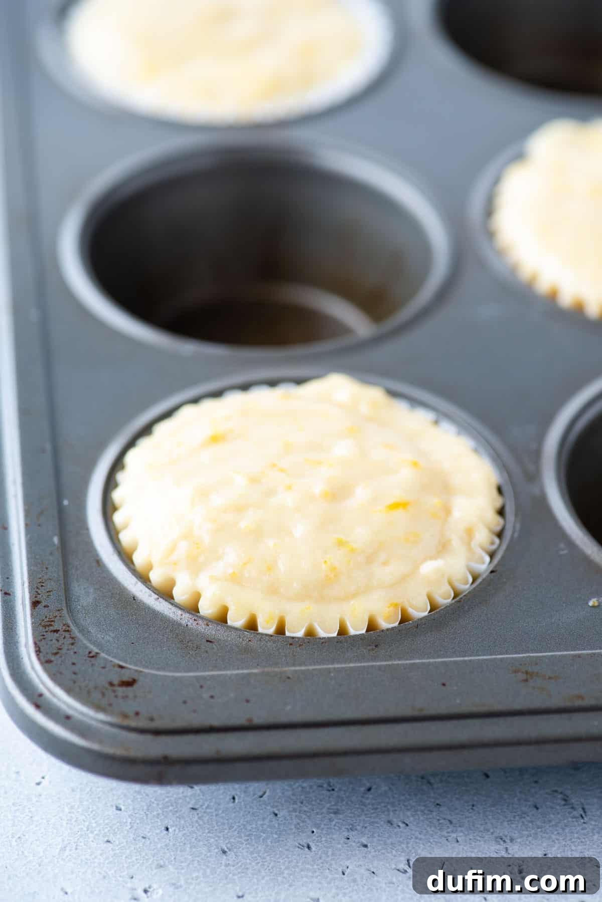 Thick orange muffin batter expertly scooped into every other well of a 12-cup muffin pan, ready for baking to achieve perfect domed tops.