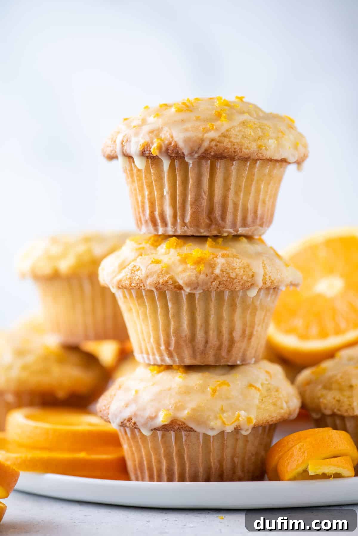 A delightful stack of three golden-brown orange muffins, showcasing their fluffy texture and enticing aroma, set against a clean white background.
