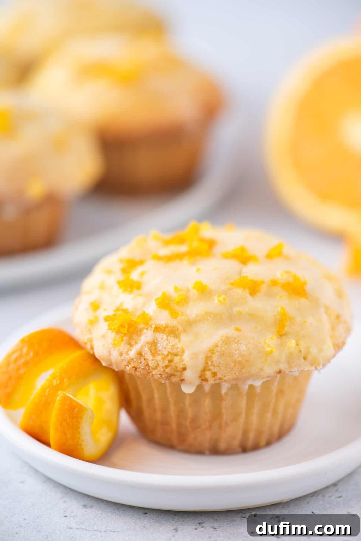 A single, beautifully baked orange muffin, light and fluffy, presented on a white plate with a subtle shadow, ready to be enjoyed.