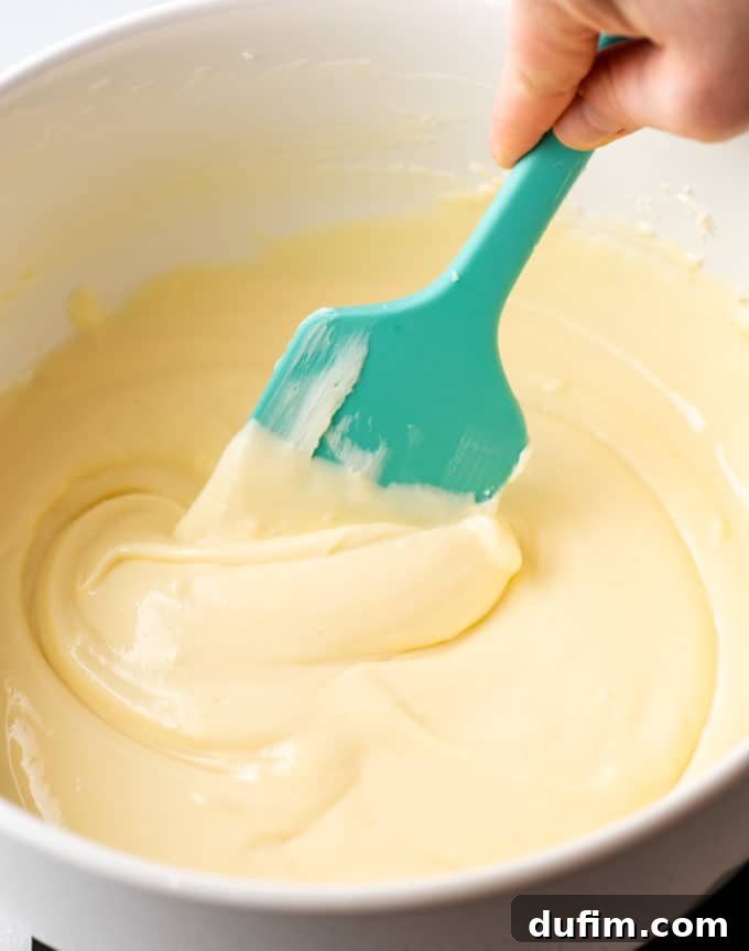 Cheesecake batter being spooned into muffin liners with graham cracker crusts.