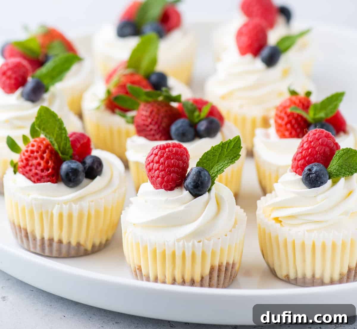 Serving tray of mini cheesecakes garnished with whipped cream, fresh berries, and mint leaves, ready for a party.