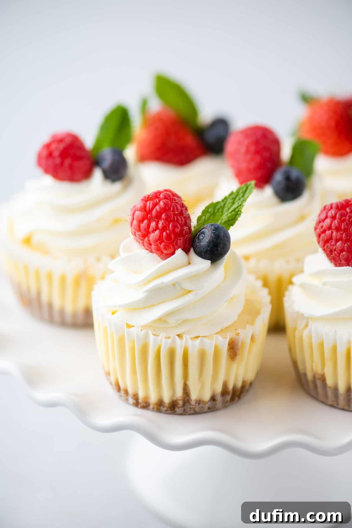 Cheesecake cupcakes on white scalloped-edged cake stand, showcasing their elegant presentation.
