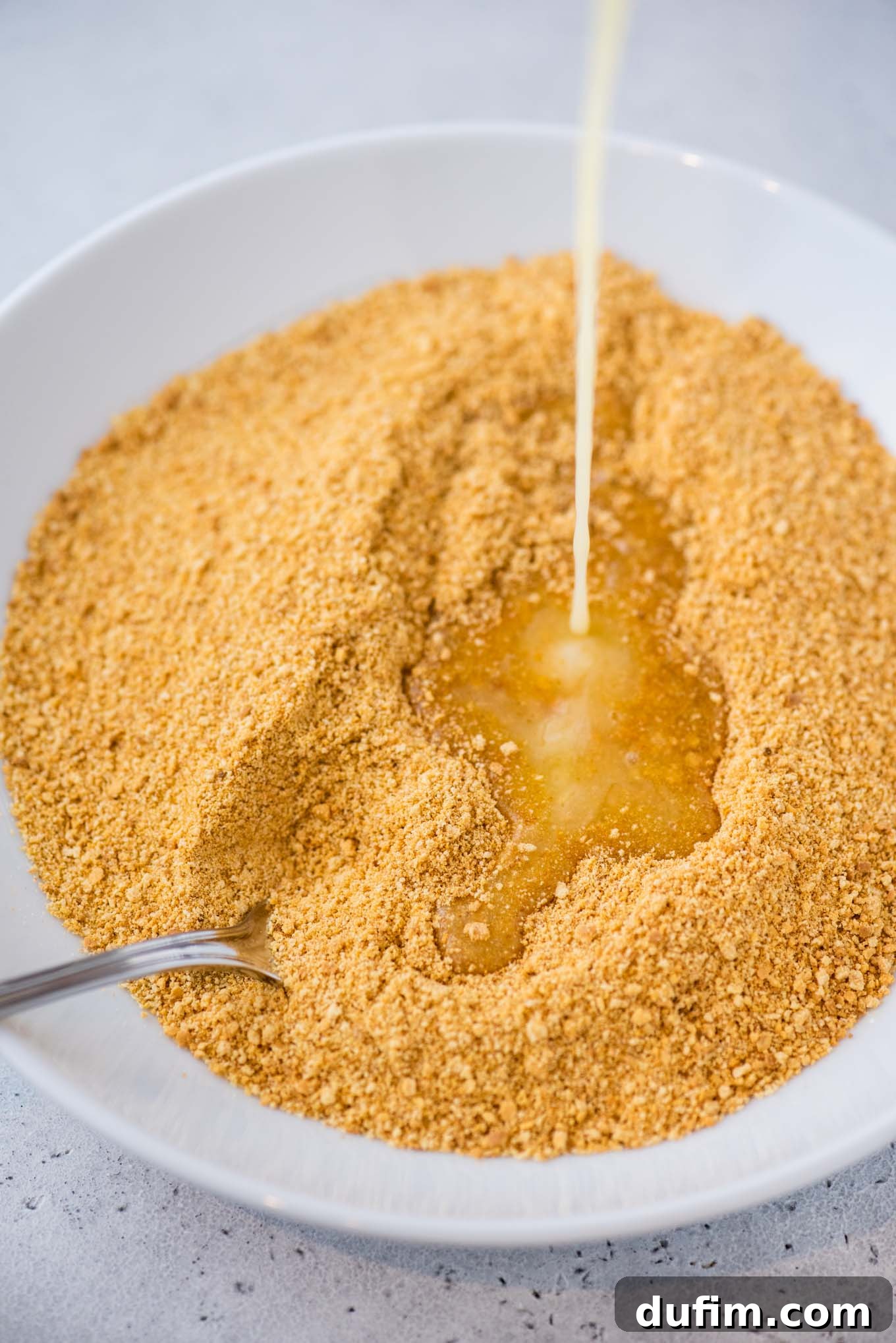 Close-up of graham cracker crumbs being mixed with melted butter in a bowl.
