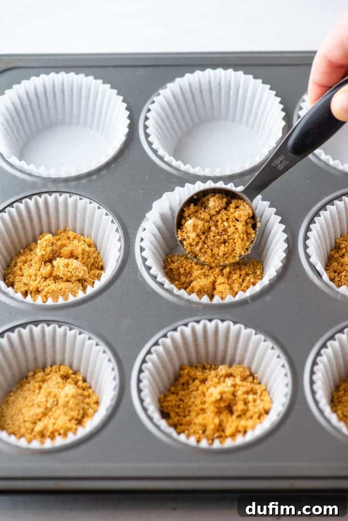 Graham cracker crust being pressed into muffin liners.