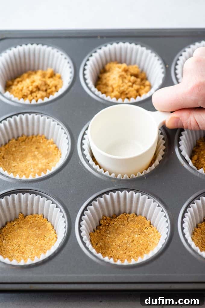 Muffin pan with pre-baked graham cracker crusts, cooling on a wire rack.