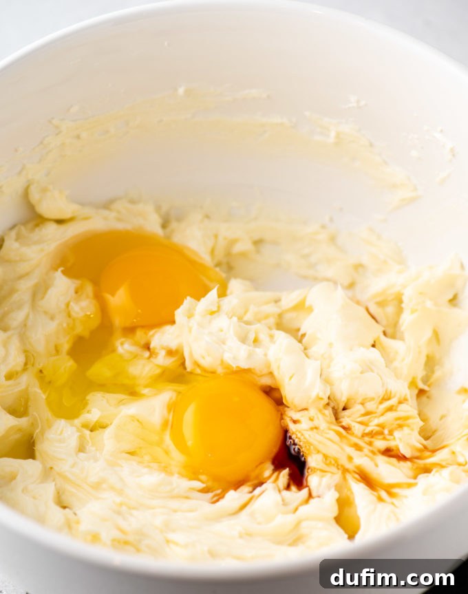 Cream cheese and sugar being beaten together in a mixing bowl with an electric mixer.