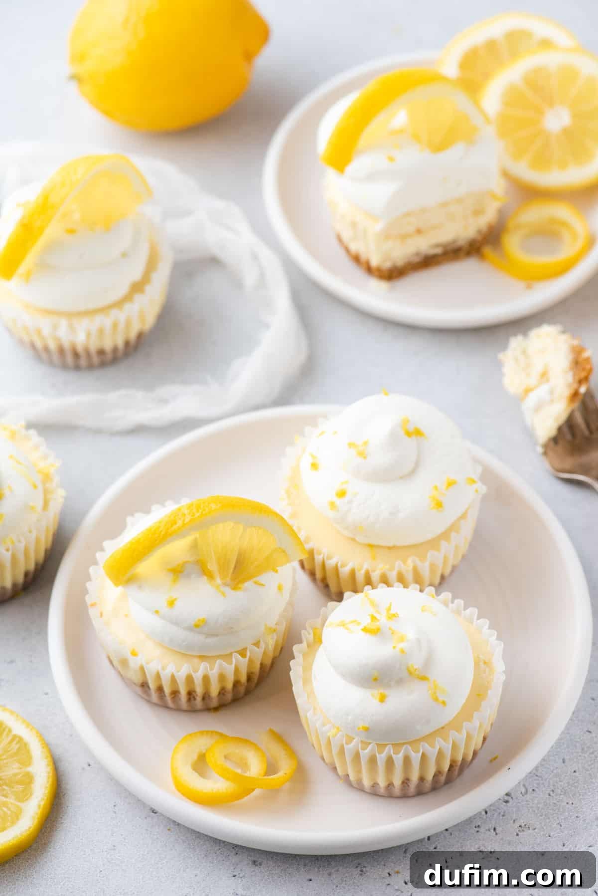 Zesty Lemon Cheesecake Bites 3 Mini lemon cheesecakes topped with whipped cream and lemon zest arranged on white plates