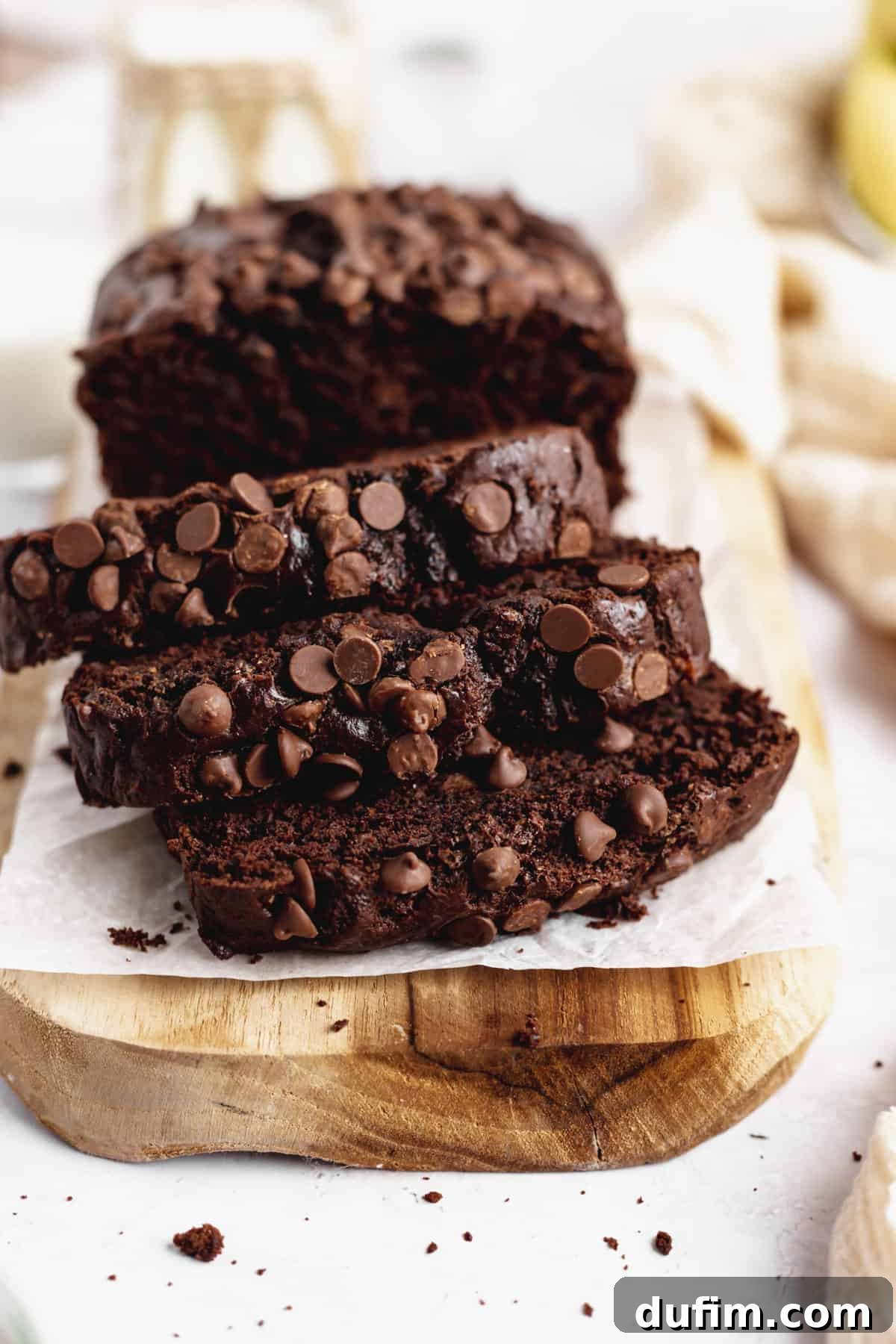 Three perfectly sliced pieces of moist Double Chocolate Banana Bread arranged beautifully on a rustic wooden cutting board, showcasing its rich texture and chocolate chips.