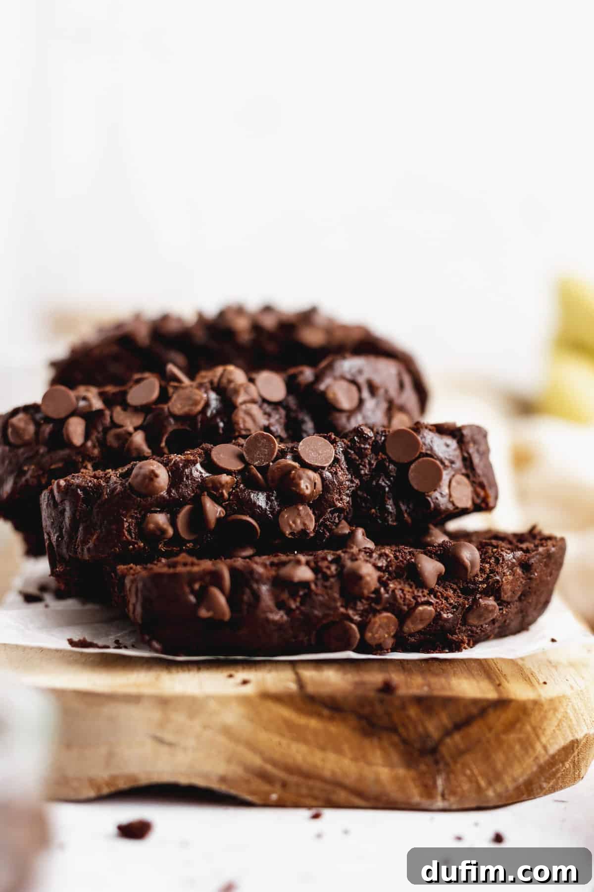 Three generous slices of moist Double Chocolate Banana Bread on a wooden cutting board, highlighting the abundance of chocolate chips.