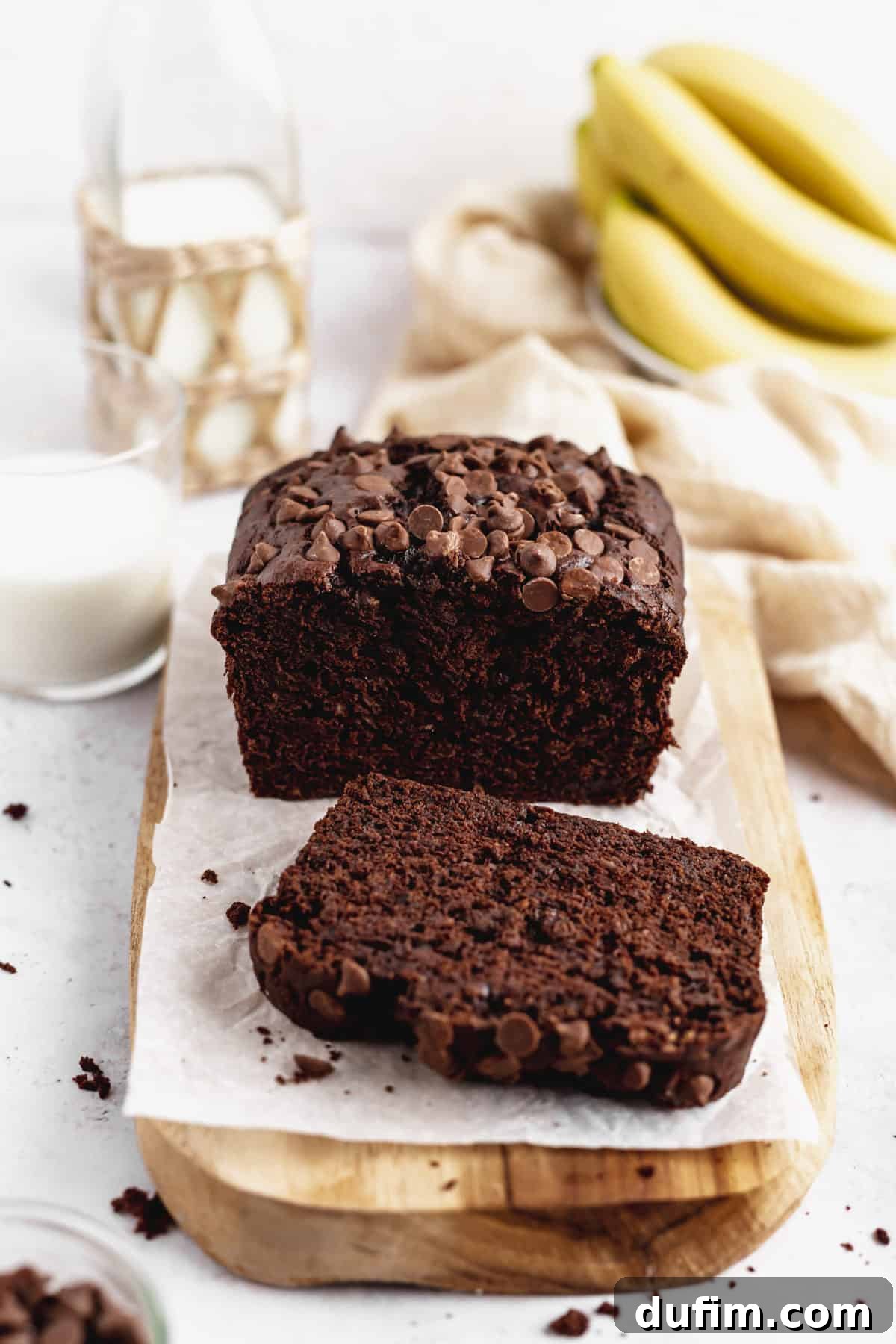 A warm loaf of Double Chocolate Banana Bread on a cutting board with a single slice cut and presented, highlighting its moist interior and generous chocolate distribution.