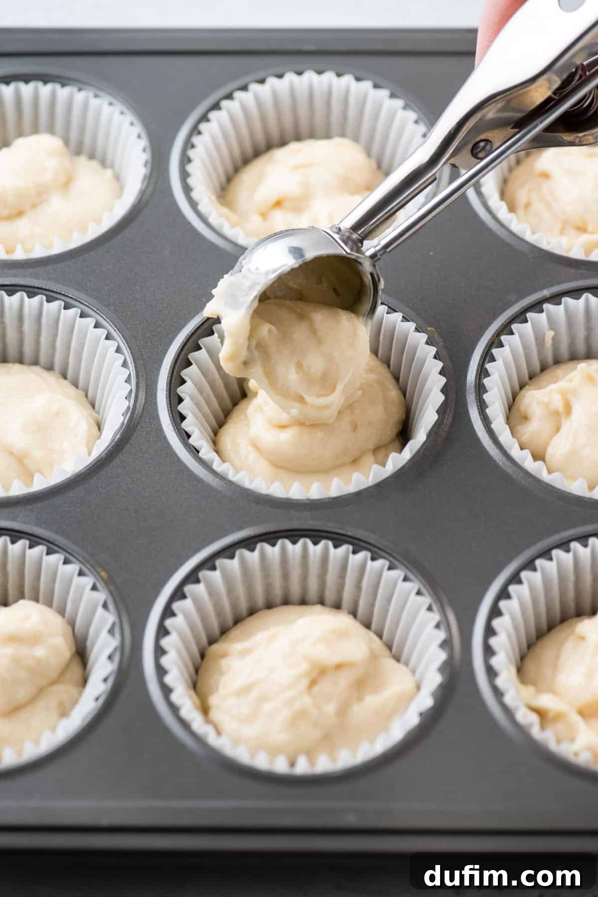 The meticulous process of portioning perfectly mixed cupcake batter into individual liners, ready for baking.