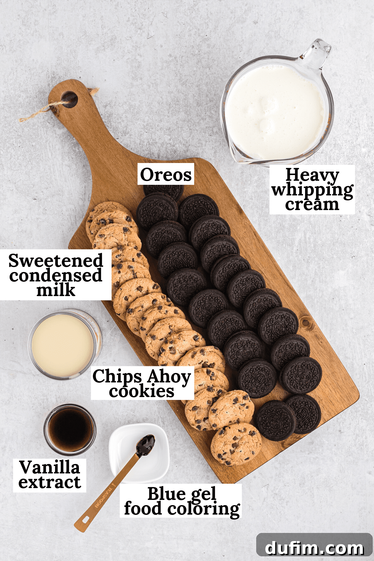 An overhead view of all the essential ingredients laid out for making Cookie Monster Ice Cream, including heavy cream, condensed milk, cookies, vanilla, and blue food coloring.