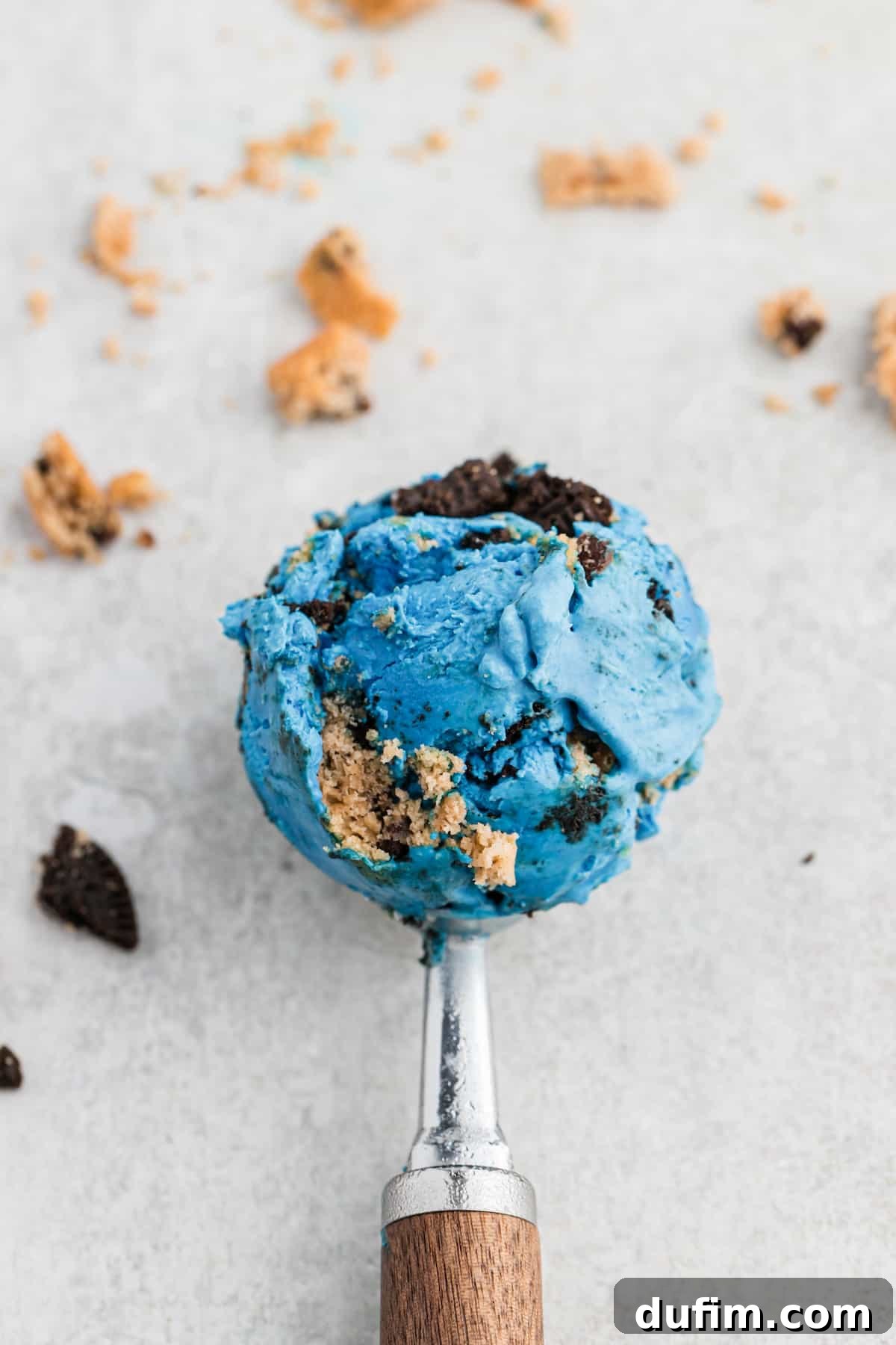 An ice cream scooper holds a perfect scoop of vibrant blue Cookie Monster Ice Cream, ready to be served.