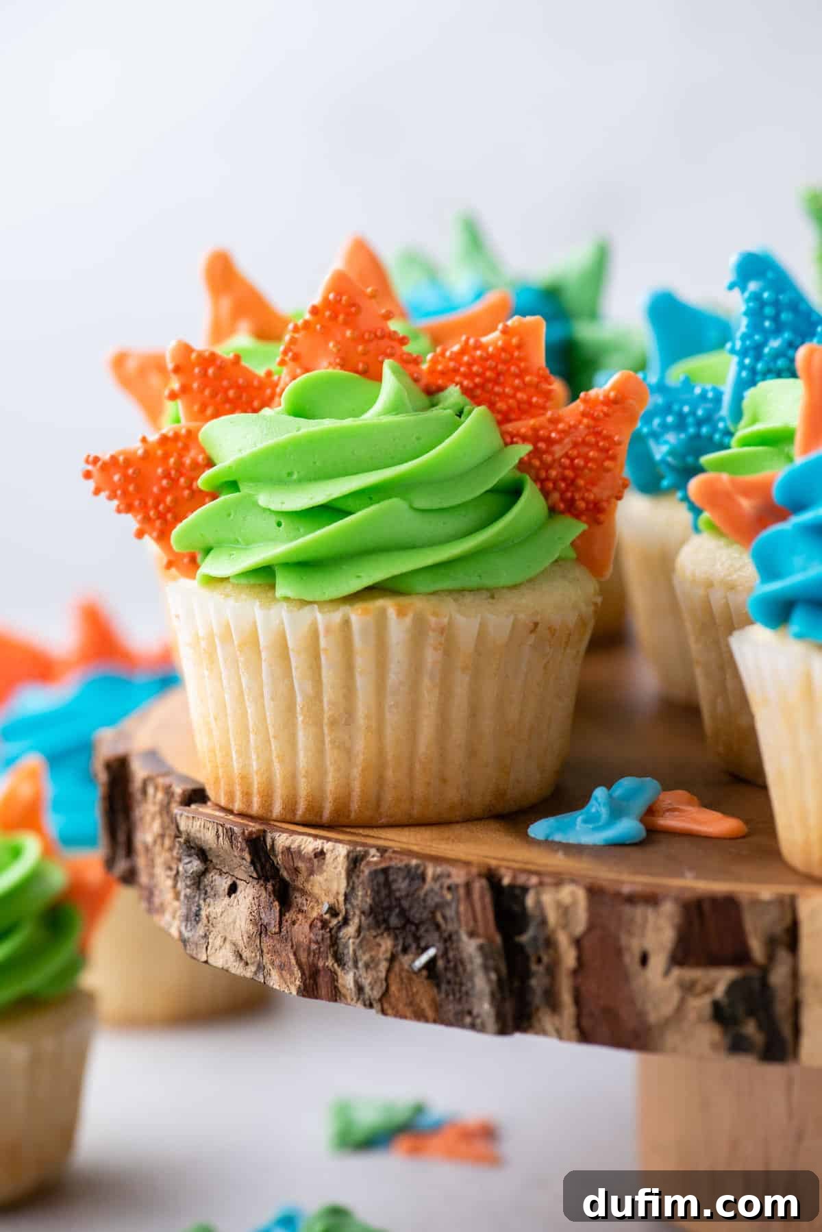 Dinosaur cupcakes arranged on rustic log cake stand