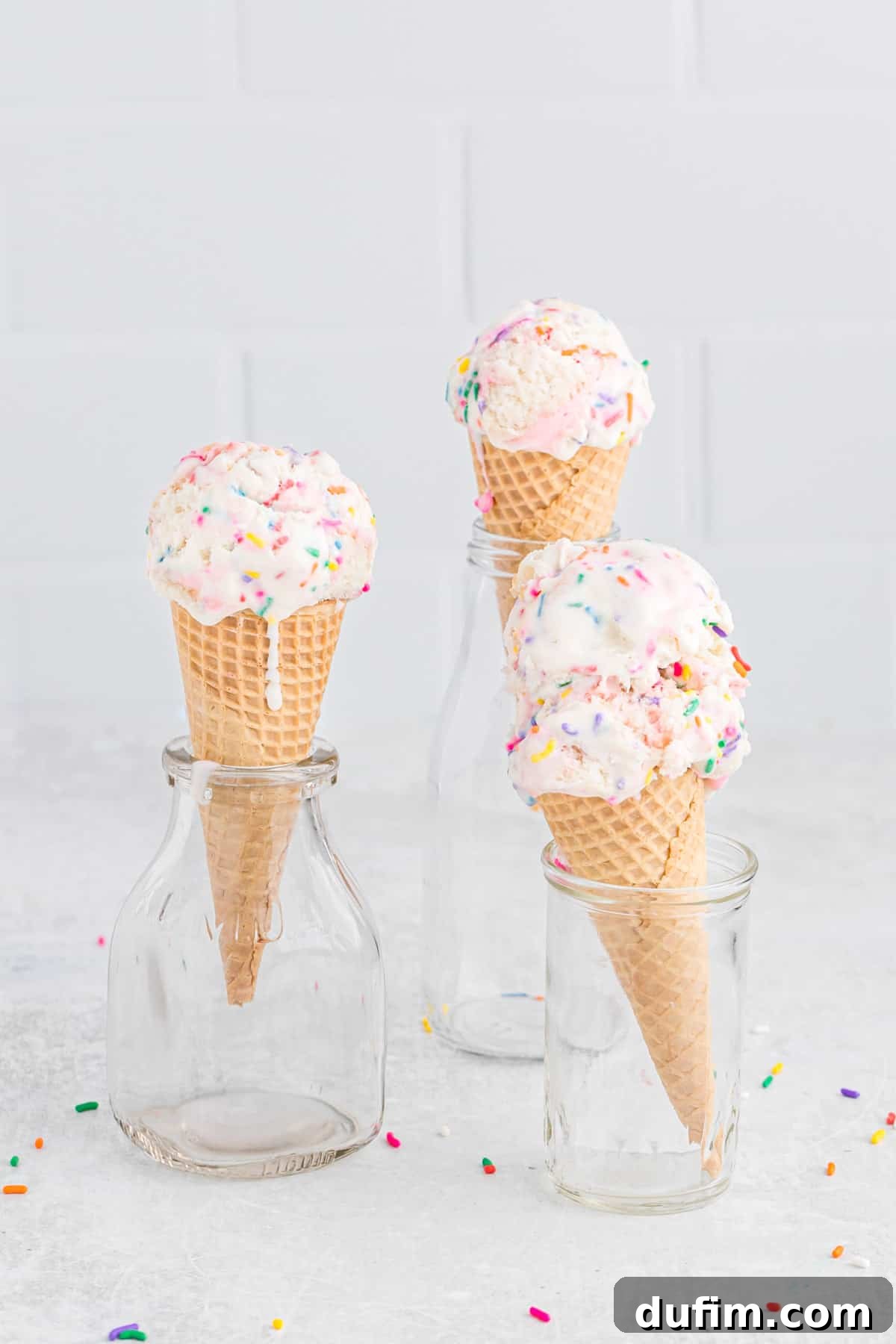 This no-churn Birthday Cake Ice Cream is loaded with colorful sprinkles and cupcakes! So easy to make, and you don't need an ice cream maker! Three ice cream cones filled with birthday cake ice cream, presented in glass jars.