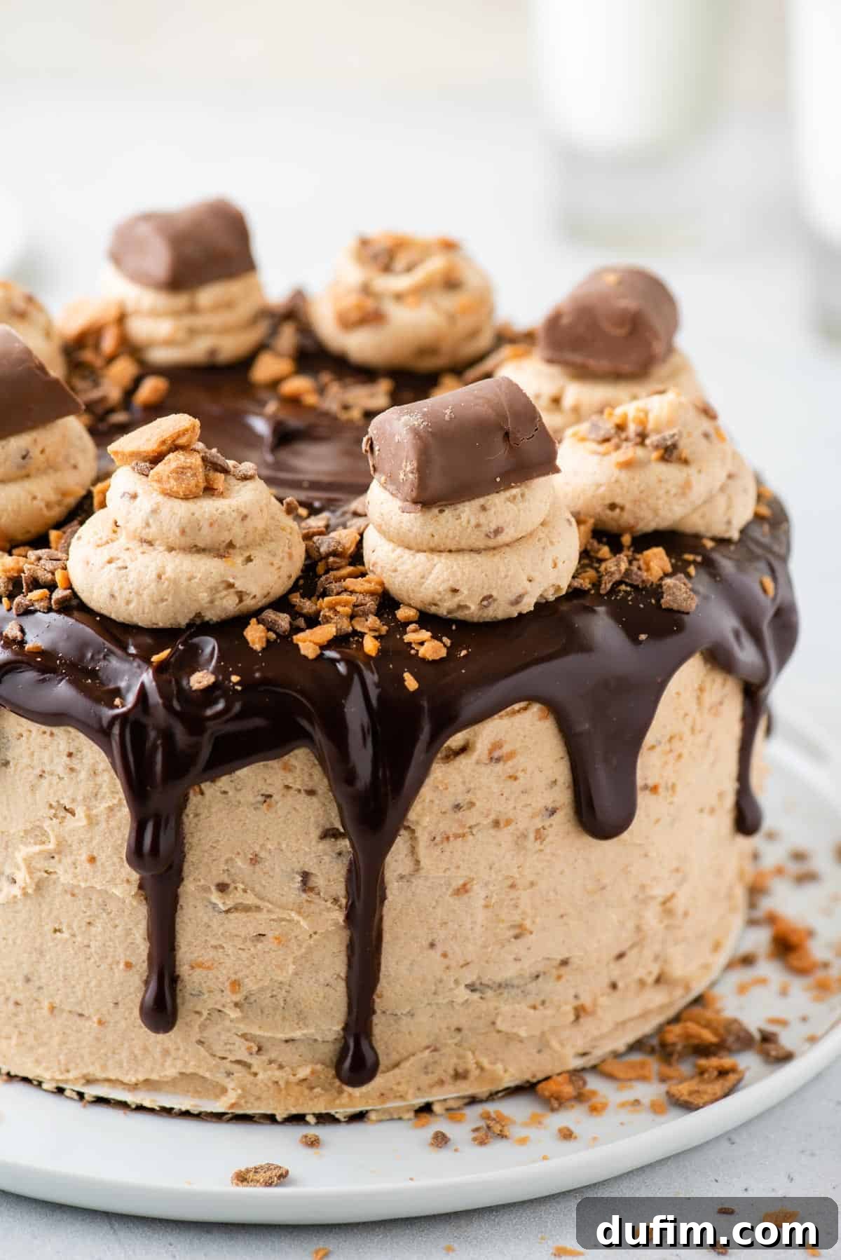 The fully assembled Butterfinger cake, showcasing its beautiful layers of chocolate cake and peanut butter cream cheese frosting, elegantly topped with a chocolate ganache drizzle and plenty of chopped Butterfinger candy.