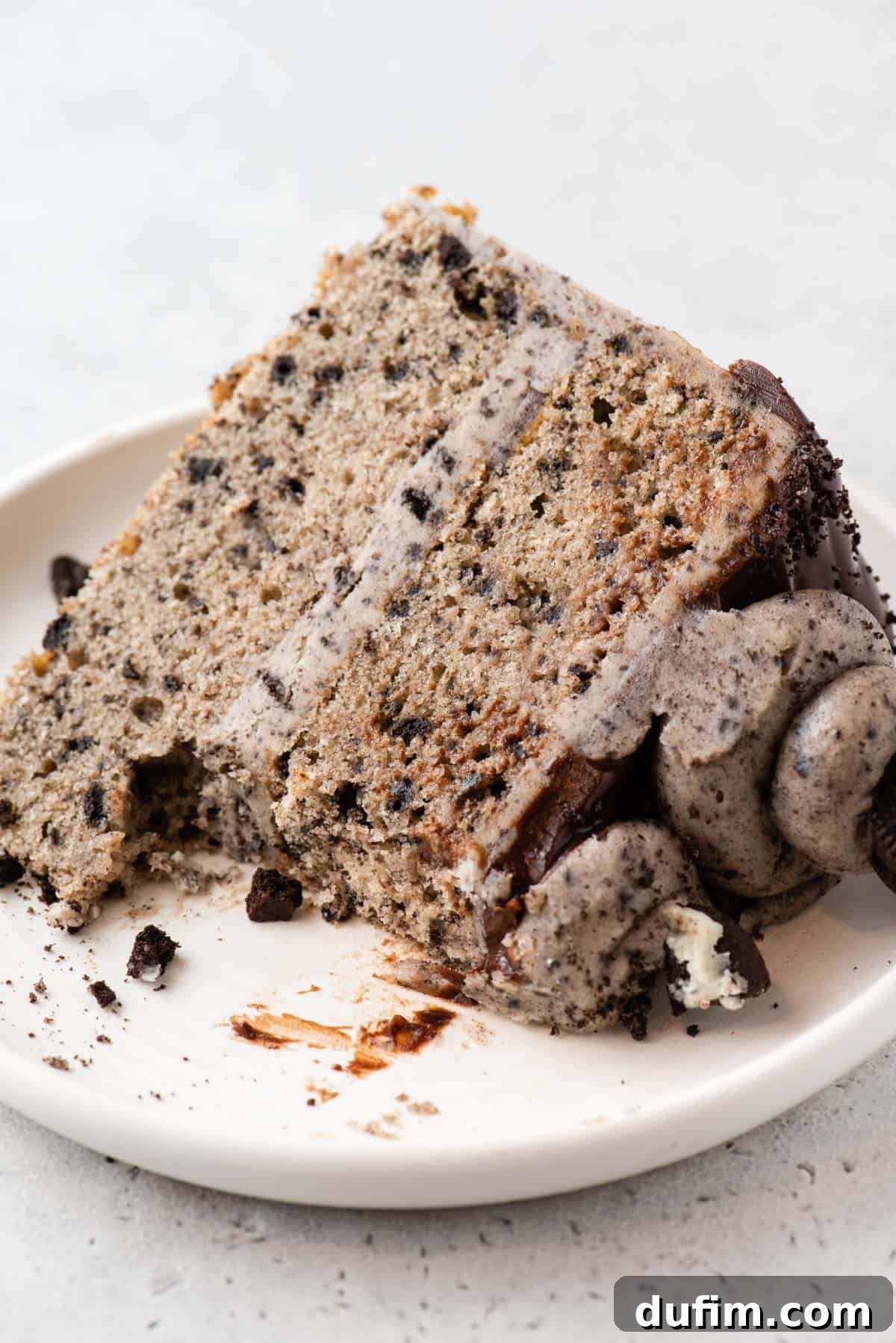 A close-up shot of a single slice of Oreo cake on a white plate, with a fork next to it, showing the moist layers and rich frosting.