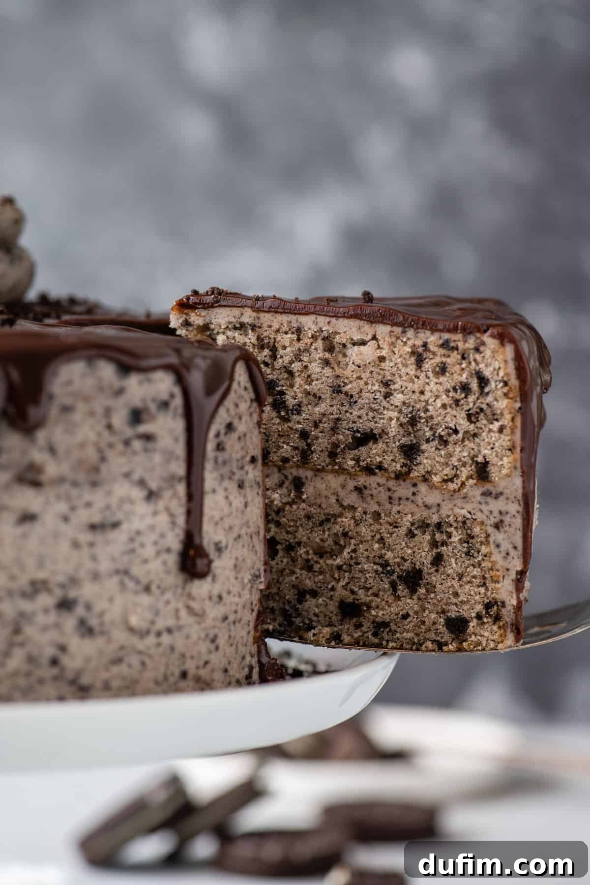 A hand gently removes a perfect slice of the rich Oreo layer cake from the whole cake, showcasing its inviting layers.