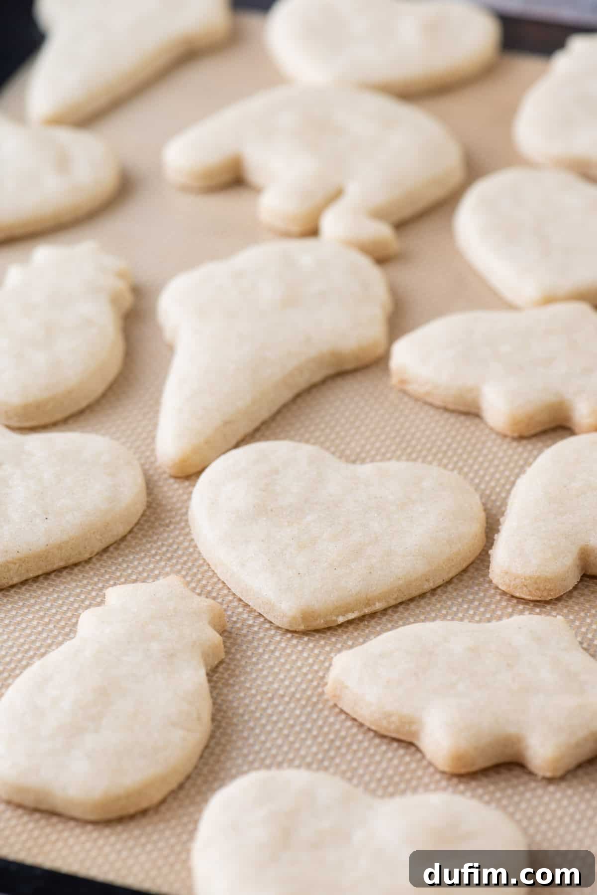 Freshly baked gluten-free sugar cookies cooling on a silicone baking mat-lined baking sheet, showing their perfectly retained shapes after coming out of the oven.