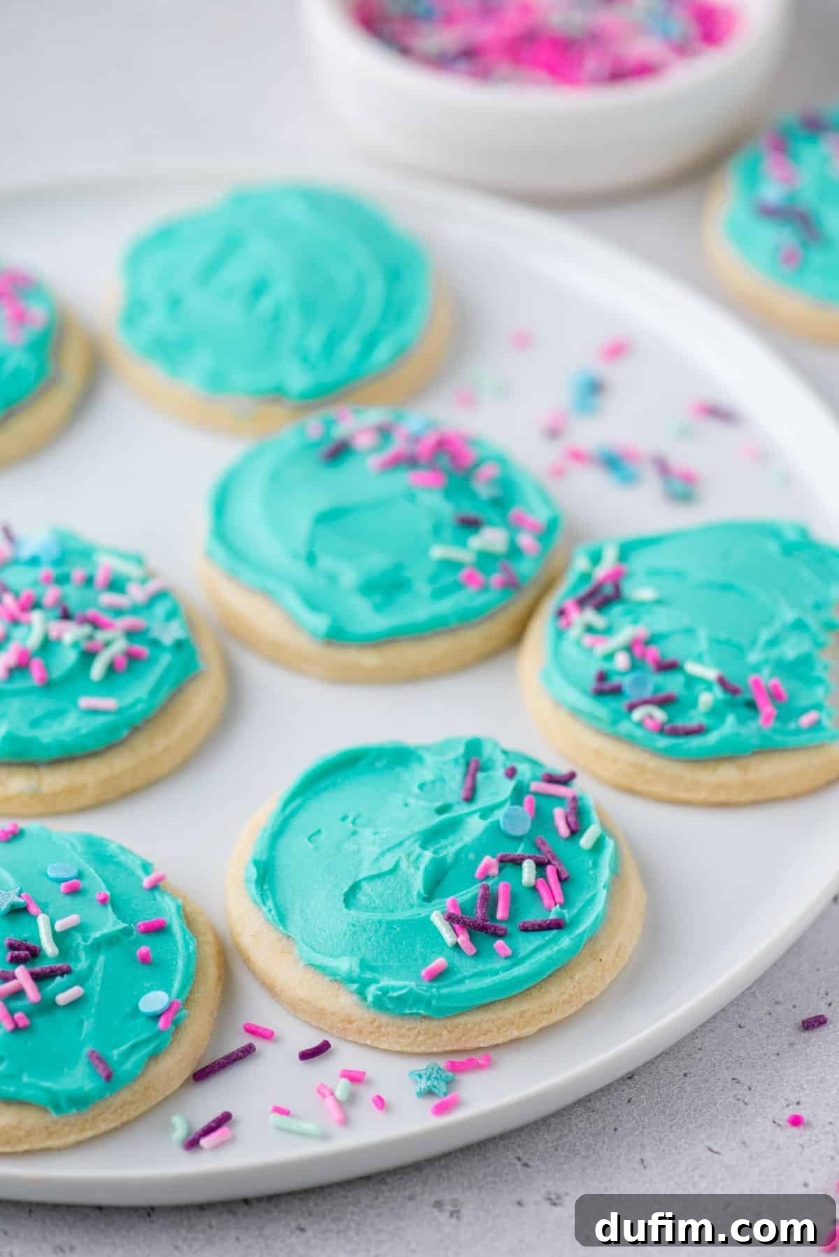 Close-up of perfectly round gluten-free sugar cookies adorned with delicate aqua blue frosting and colorful sprinkles, beautifully arranged and ready to be enjoyed.