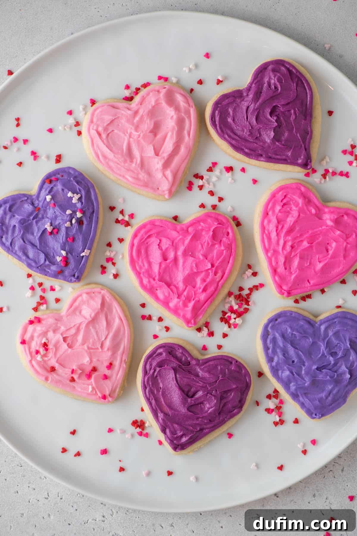 Overhead shot of beautifully arranged heart-shaped gluten-free sugar cookies, some decorated with delicate pink frosting and colorful sprinkles, perfect for a special occasion like Valentine's Day.