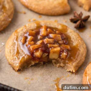 Closeup of a bitten apple pie cookie revealing the soft texture, spiced apple filling, and caramel drizzle, indicative of a perfect fall treat.