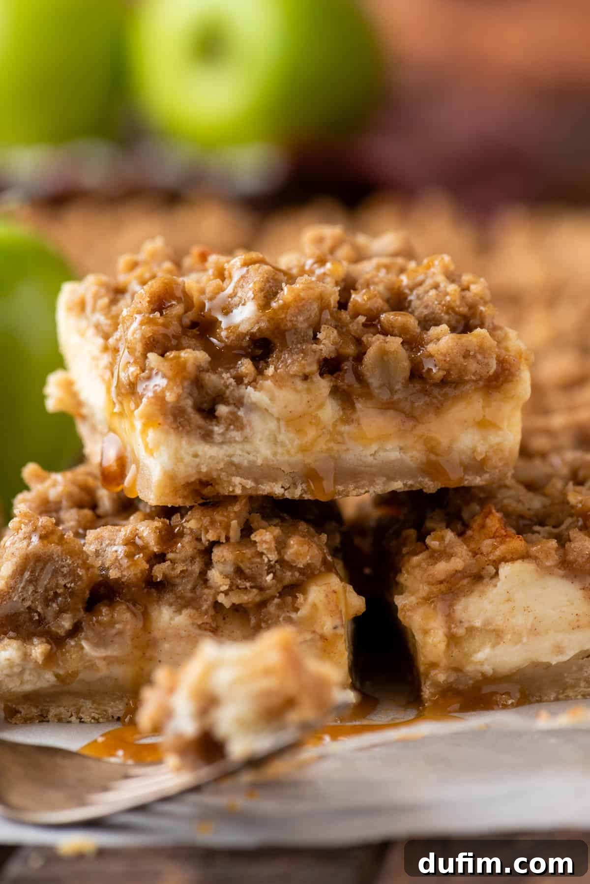 Stack of 3 caramel apple cheesecake bars, showcasing the distinct layers of crust, cheesecake, apples, and streusel, with a generous caramel drizzle.