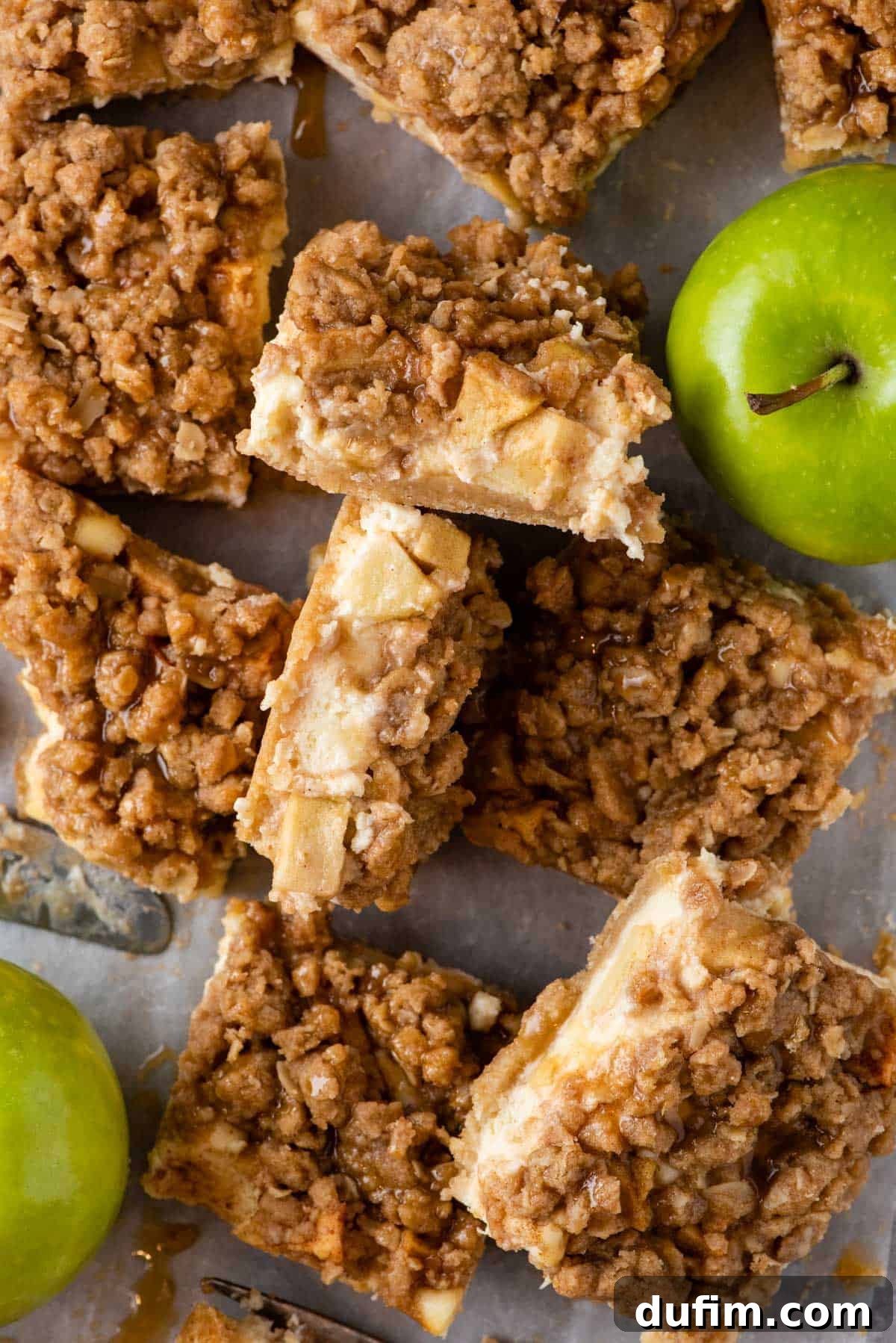 Overhead view of several caramel apple cheesecake bars artfully arranged with whole green apples, highlighting the rustic yet elegant presentation.