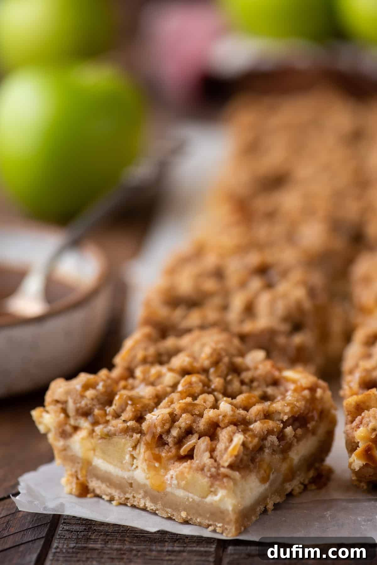 Close-up shot of caramel apple cheesecake bars, freshly baked and still on parchment paper, ready to be cut and served.